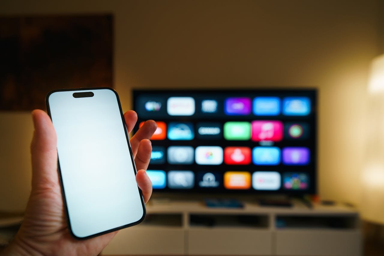 hero-img-01 A smartphone in focus with a smart TV displaying apps in a cozy living room.